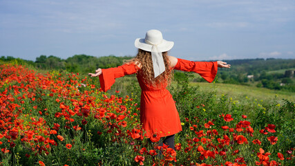 woman in a poppy field, girl in red dress and hat stands with her face turned away from the camera with open arms