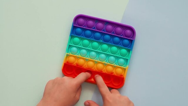 KId hands play with popit or simple dimple toy, top view over two-shadows blue background. Popit game on blue background. Popular silicone colorful antistress pop it toy in child hands. POV shoot