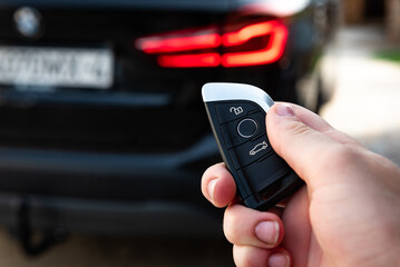 Fototapeta premium Hand holding a car key with remote control and pushing a button, he is unlocking the door.