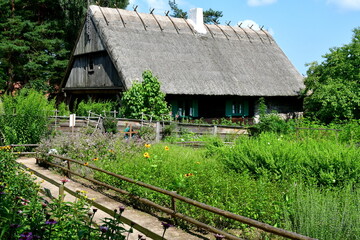 Fototapeta na wymiar A view of a small abandoned shelter, hut, or house with an angled roof and with a dirt path leading to it with a lush garden growing on both sides seen on a cloudless summer day in Poland