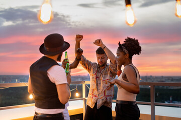 Group of young people dancing and having beer at party on rooftop patio