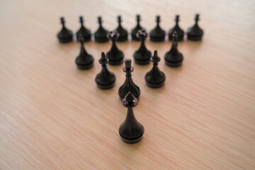 black chess pieces arranged in the shape of a pyramid on a wooden surface