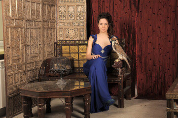 young girl in a blue dress in a vintage interior with a falcon on her hand