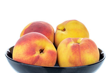 Four ripe peaches in a black ceramic bowl, close-up, isolated on white.