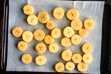 Sliced Plantains on a Parchment Covered Sheet Pan: Slices of raw cooking bananas on a baking sheet