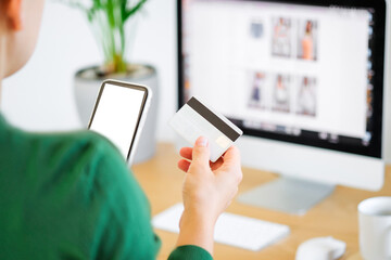 unrecognizable woman holding a credit card and white screen smartphone in front of the laptop computer screen, Online shopping and secure online payment concept