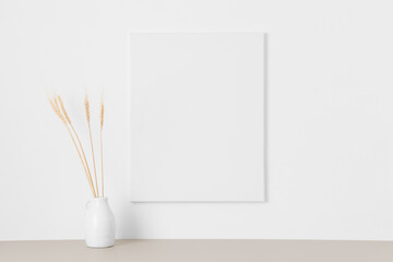 White canvas mockup on the wall with a dried flower decoration.