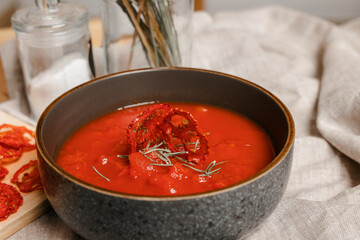 dried tomatoes on a wooden board and red soup. Tomato chips. Tomato soup in a black bowl on the background of a wooden table. Fabric napkins made of linen. A glass salt shaker. 