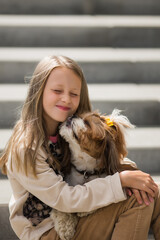 Portrait of beautiful preteen girl petting and hugging shih tzu dog looking at the camera outdoors.