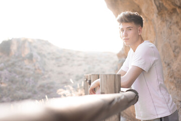 Chico joven rubio sonriendo haciendo senderismo junto a las montañas en la puesta de sol