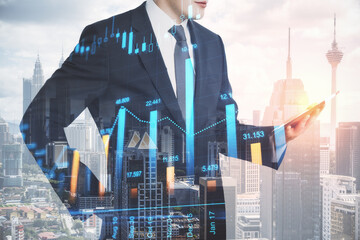 Attractive young european businessman with tablet standing on abstract city background with forex chart. Trade and communication concept. Double exposure.