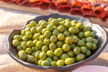 Green pickled olives are lying in a metal bowl.