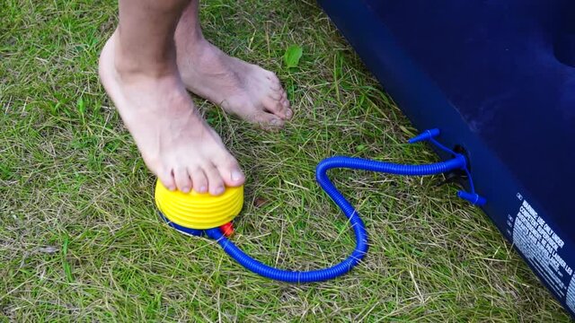 The inflatable mattress is pumped with a foot pump. The man will inflate the mattress with his foot while standing on the grass.