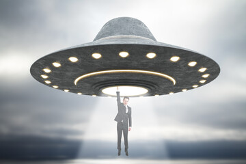 Abstract grey UFO taking businessman in dull sky. Spaceship, kidnapping and science concept.