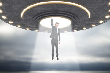 Abstract grey UFO taking businessperson in dull sky. Spaceship, kidnapping and science concept.