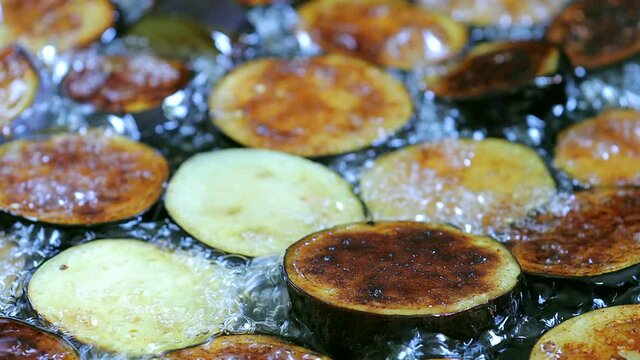 Vegetable fry in sunflower oil . Frying chopped eggplant in the pan . Sliced eggplant fried in a black frying pan . Professional chef mixing vegetables with a spatula . Oil splashes . Frying bubbles .