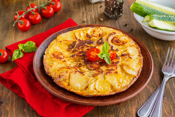 Spanish tortilla, traditional dish with eggs and fried potatoes on a clay plate on a wooden background. Potato recipes.