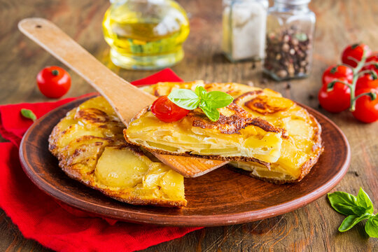 Spanish tortilla, traditional dish with eggs and fried potatoes on a clay plate on a wooden background. Potato recipes.