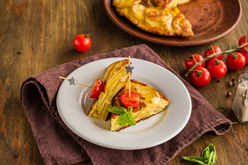 Sliced Spanish tortilla, a traditional dish with eggs and fried potatoes on a clay plate on a wooden background. Potato recipes.
