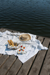 The concept of a romantic holiday. Picnic on the pier against the background of the river. Baguette in a jute basket. Champagne glasses. fruits, apricots and pears. wooden board and white sheet