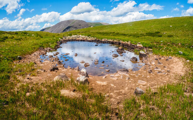 Green swampy plateau and a blue puddle against the background of distant hilly mountains. A panorama of a pure green landscape.
