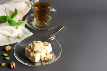 Halva with pistachios on a glass plate on a dark background. Turkish, Arab and Jewish national sweets. Natural vegan product. Traditional oriental dessert Chekme. Copy space.