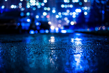 Rainy night in the big city, alley with cars on the background of glowing windows of the house opposite. View from the level of asphalt