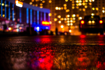 Rainy night in the big city, light from the shop windows and the windows of the house is reflected in the asphalt. View from the level of asphalt