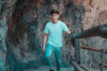 Chico joven serio junto a las escaleras posando entre las rocas y montañas