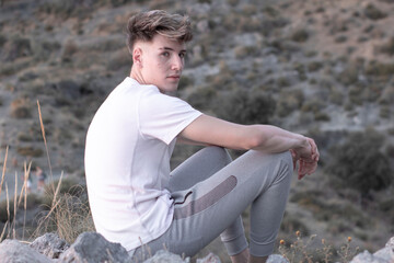Chico joven en las montañas junto a la vegetación mirando con seriedad