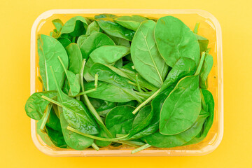 Fresh Baby Spinach Leaves in Transparent Plastic Package on Yellow Background - Top View. Vegan and Vegetarian Culture. Raw Food, Green Leaves. Healthy Diet