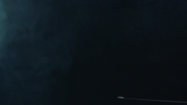 Professional fencer in protective uniform practicing maneuvers with sword alone in dark studio . Fencing demonstration on black smoked background . Shot on Arri Alexa cinema camera in slow motion .