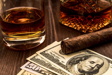 Decanter of whiskey and a glass with cuban cigar and money on a wooden table. Angle view, focus on...