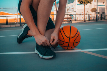 Jugador de baloncesto junto con el balon en la pista atandose los cordones para prepararse en el...