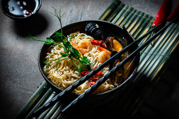 Traditional Japanese soup ramen with shrimp, asian noodles, mussels chili pepper on dark background. Asian style food. Space for text. Noodles with seafood and microgreen