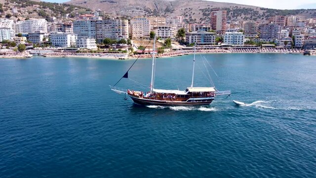 An old two-masted ship sails on the waves of the Ionian Sea against the backdrop of the city