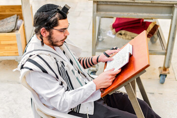 Orthodox Jewish man, wearing phylacteries (tefilin) and shawl (tallit), sitting praying at the...
