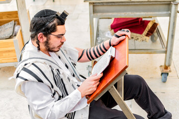 Orthodox Jewish man, wearing phylacteries (tefilin) and shawl (tallit), concentrating on studying...