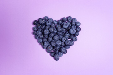 Creative food health diet holiday concept photo of valentine heart made of blueberry on purple background.