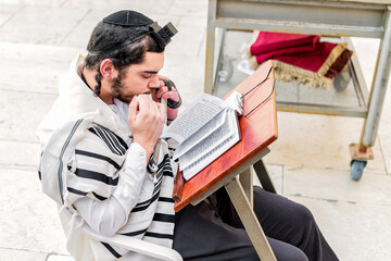 Orthodox Jewish man, with phylacteries (tefilin) and shawl (tallit), kissing the tzitziot of the mantle during prayer.