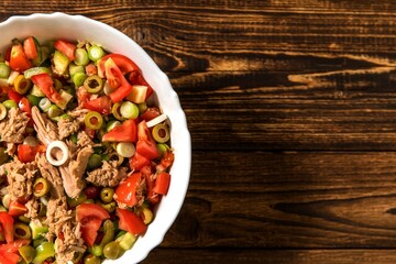 Tasty tuna salad with vegetables on wooden table. Vegetable salad with tuna. Preparing a healthy vegetable salad with fish. Diet food for athletes.
