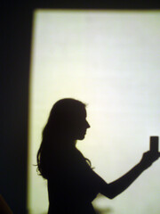 A black shadow of a woman with long loose wavy hair holding a mobile in her hand, white background