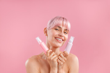 Portrait of happy young woman with pink hair holding two plastic bottles with beauty products,...