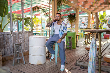 Chico joven atractivo tatuado con camisa de flores en local de playa en dia soleado de verano