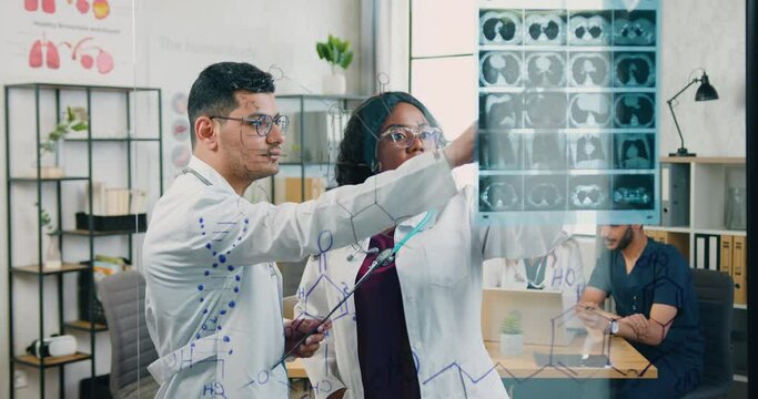 Good-looking high-skilled confident diverse male and female doctors investigating results of patient's x-ray attached to the glass wall in medical office