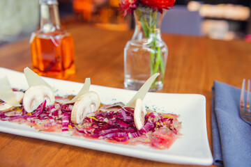 Tuna carpaccio with purple cabbage and sliced parmesan cheese. Carpaccio wooden table in restaurant. Sunny lunchtime