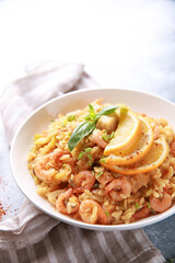 Healthy food. A seafood dish. Risotto with shrimp, scallops, lemon and fresh herbs in a white plate on a bright table. Background image, copy space