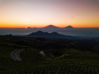 Golden sunrise view on the mountainside, slope of the Mount Sumbing. Sunrise view with vegetable plantations in clear condition weather and 4 Mountains see clearly.