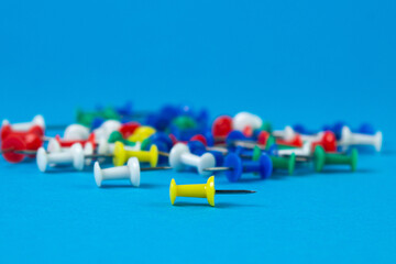 Multi-colored push pins on a blue background. Office stationery.