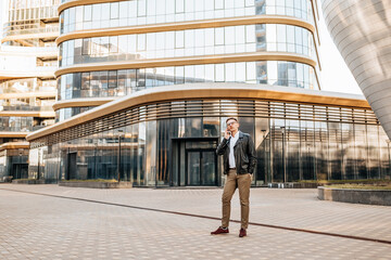 Handsome man with glasses with a smartphone on the street of a big city. Businessman talking on the phone on urban background